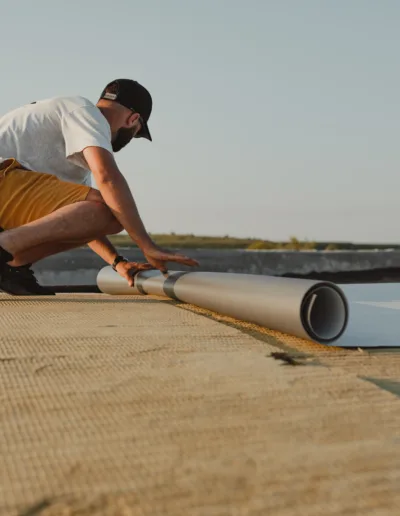 A man is working on a roof with a roll of roofing material.